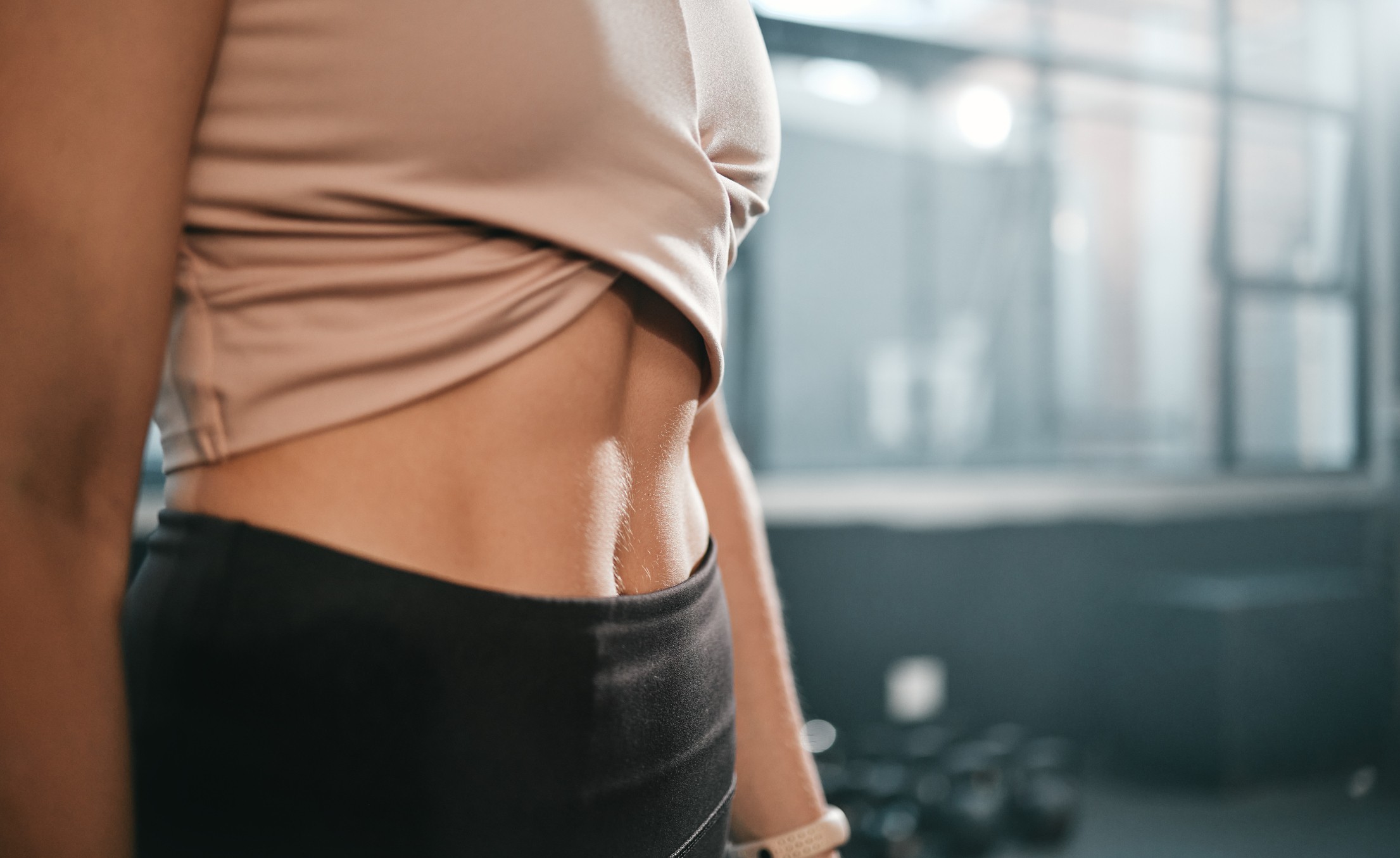 Fitness, stomach and woman in a gym for exercise, health or wellness for weightloss training. Sports, tummy tuck and closeup of a slim female athlete or model belly after a workout in a sport center.